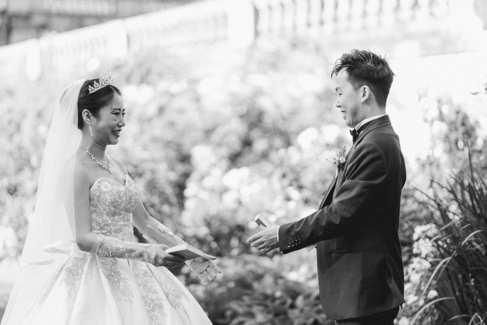 Black and white photo of a bride and groom exchanging vows in a garden setting.