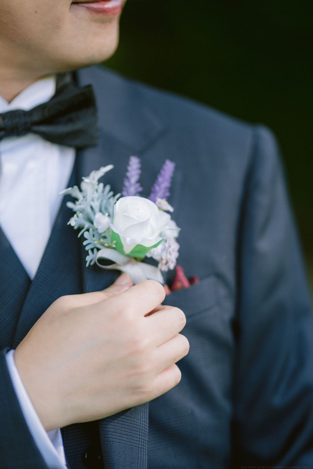 Close-up of a white rose and lavender boutonniere on a dark suit lapel.