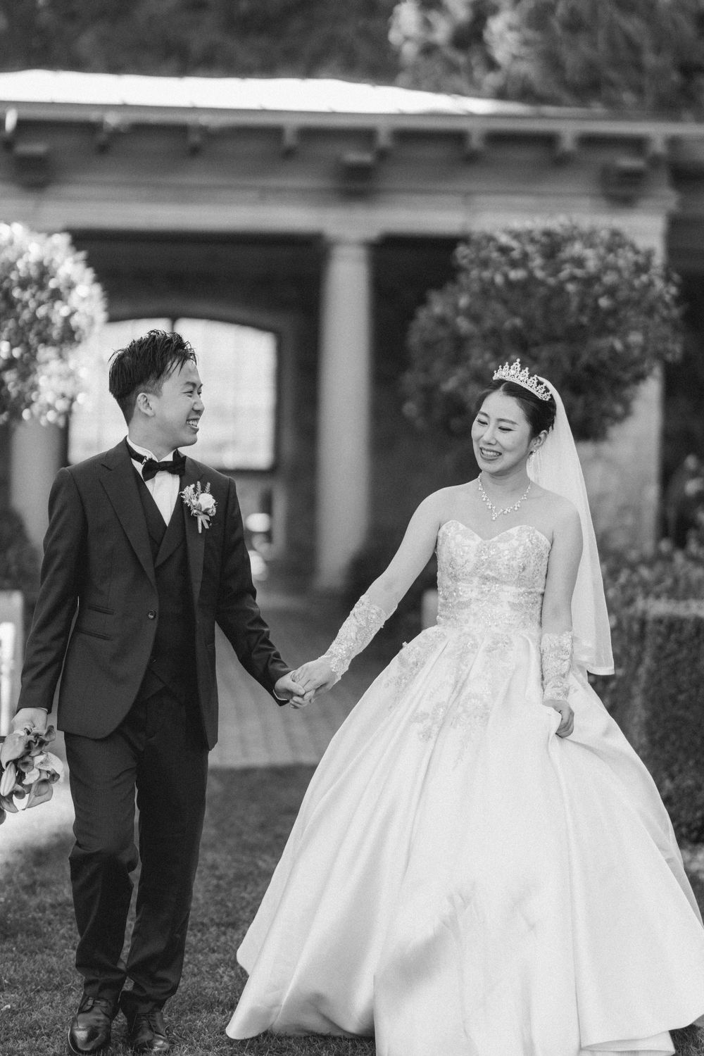 Black and white photo of a joyful couple walking hand in hand through a garden.
