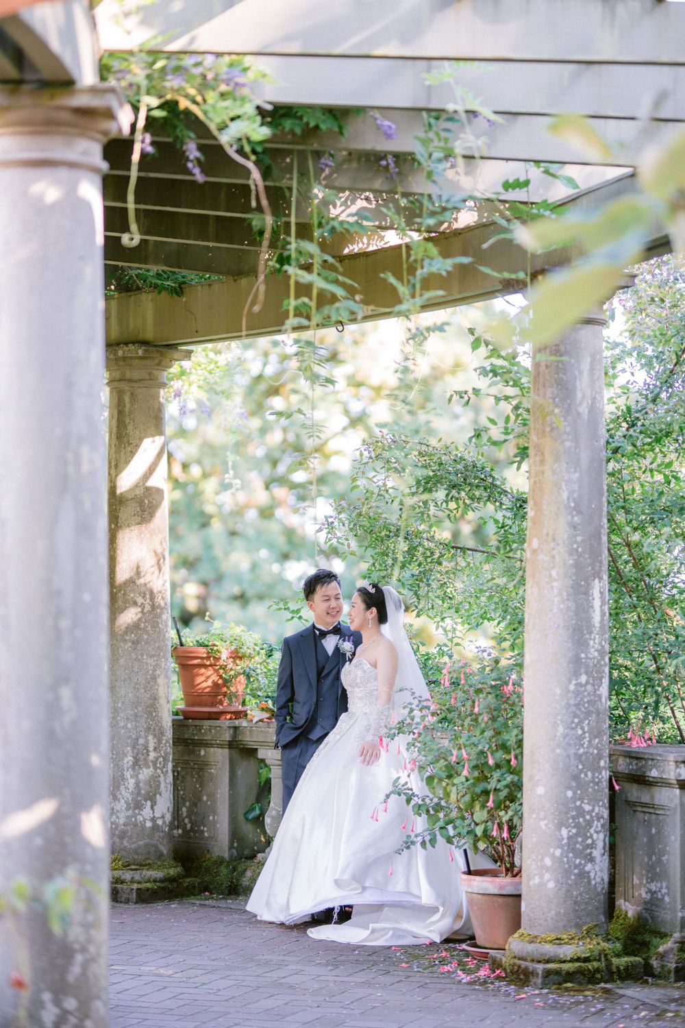 Couple shares intimate moment under garden pergola surrounded by climbing vines and flowers.