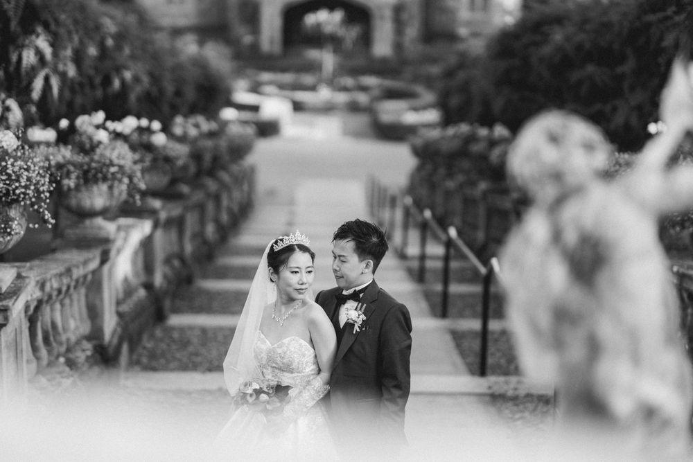 A romantic wedding portrait on an elegant stone staircase with ornate landscaping in black and white.