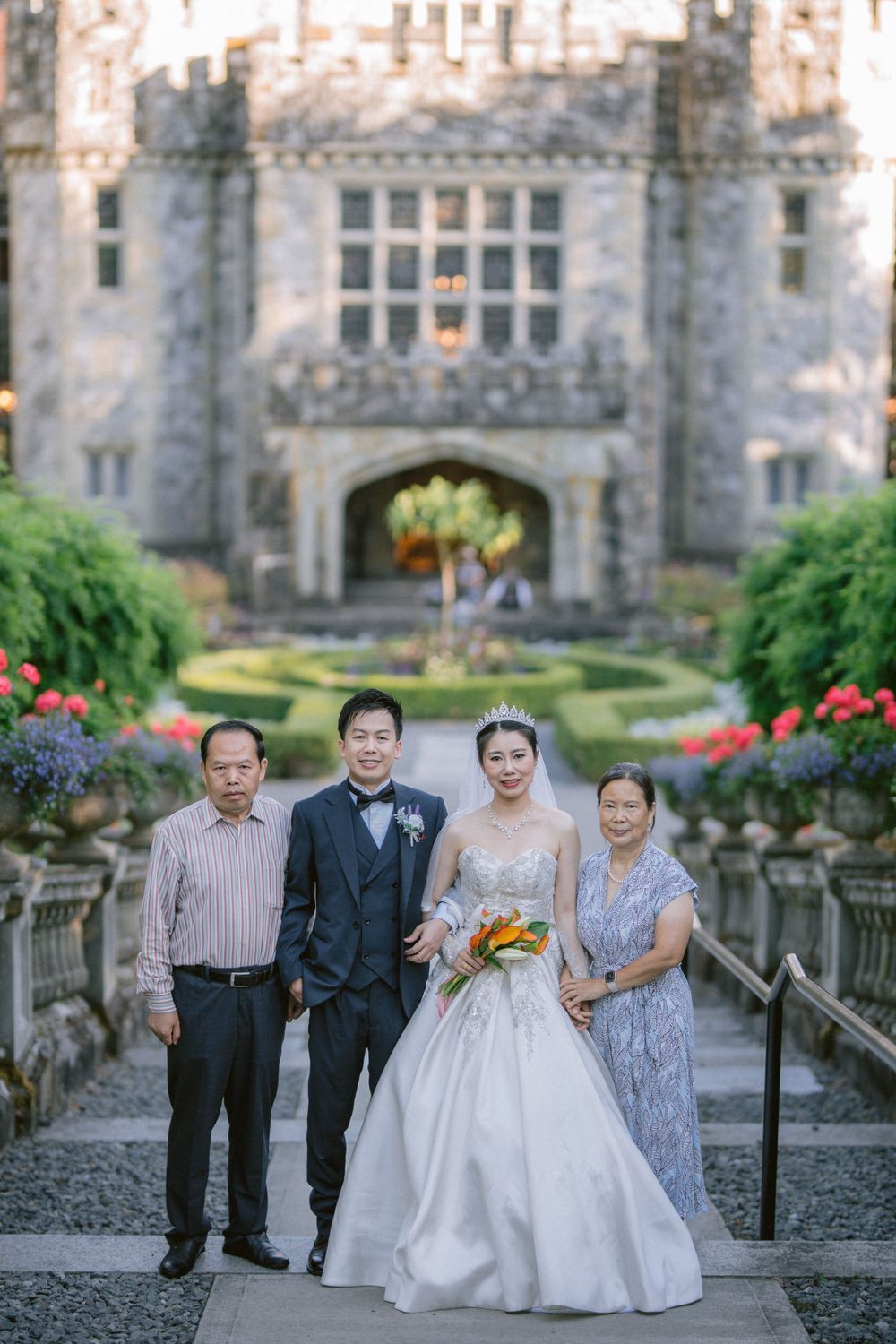 Formal wedding photo in front of a grand stone castle with beautiful gardens and architecture.