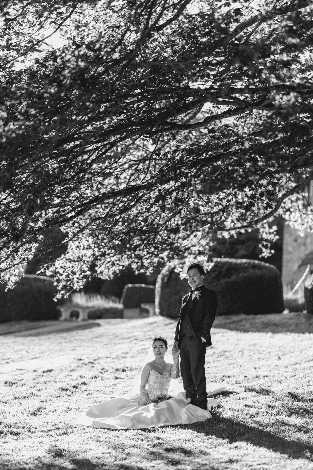 Black and white wedding portrait under flowering tree branches in afternoon light.