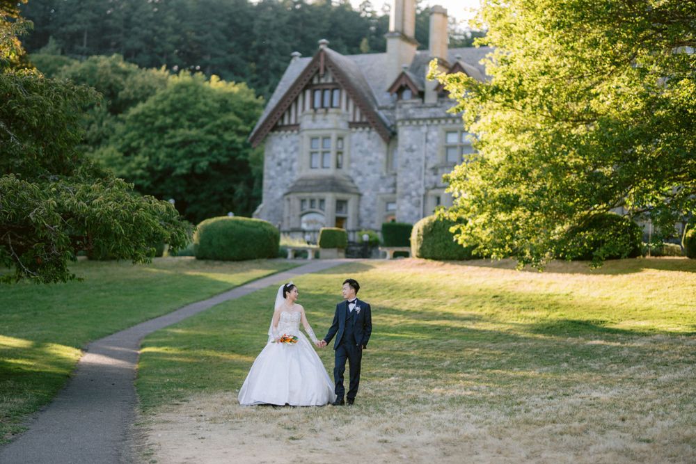 Wedding couple walking near a charming Victorian stone mansion with manicured grounds.