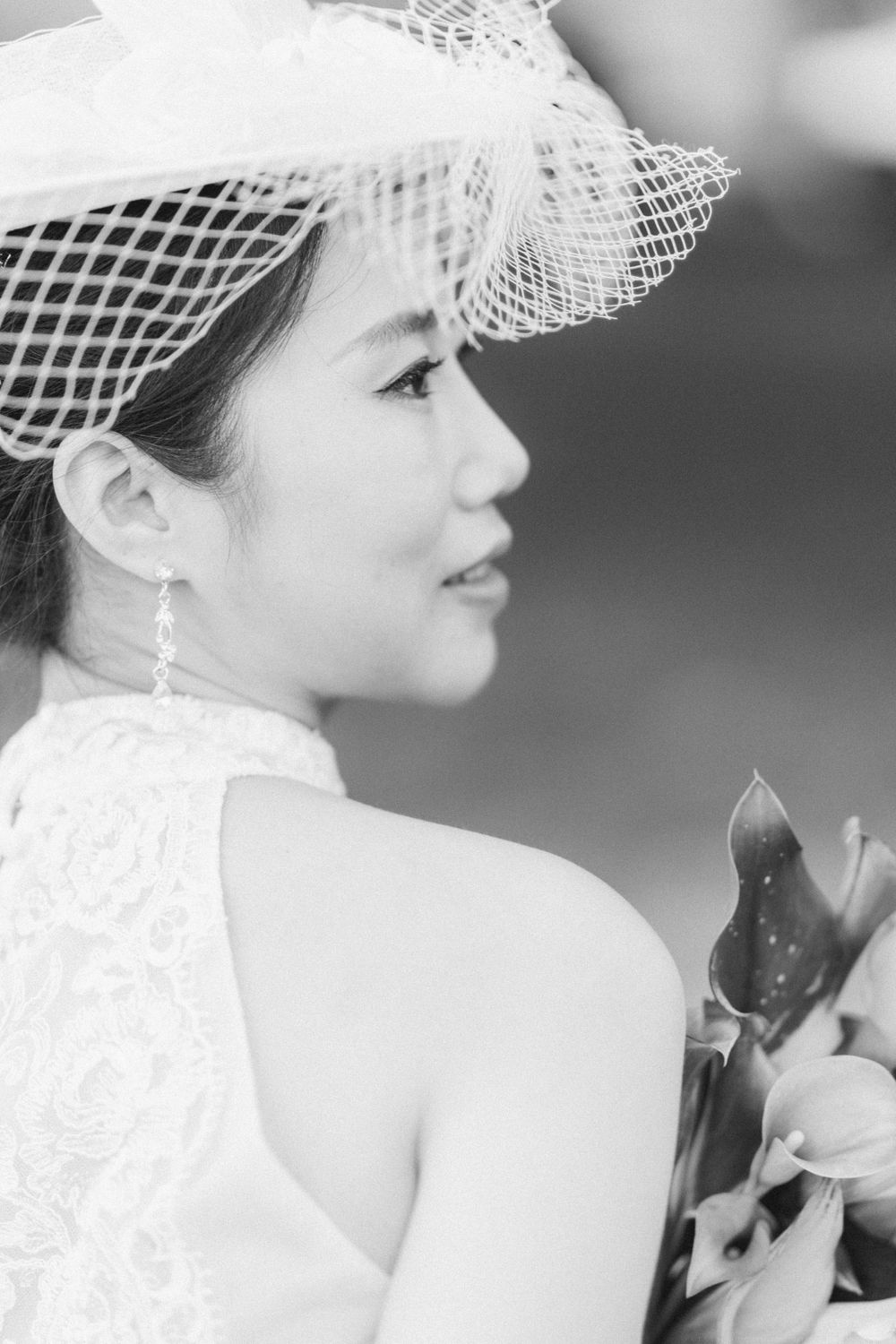 Side profile of bride wearing delicate lace dress and netted hat with floral details.