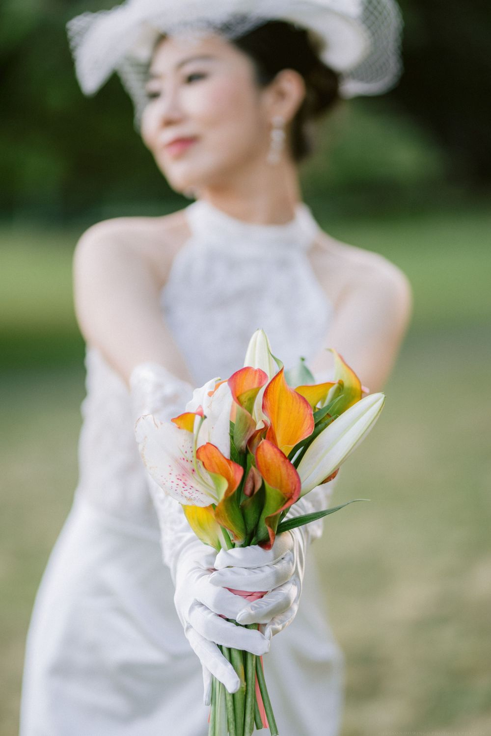Close-up of white gloved hands holding orange calla lily and white flower bouquet.