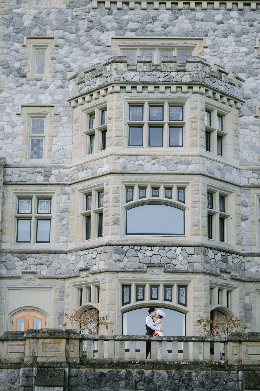 Wedding couple embracing on stone balcony of historic castle with ornate architecture.