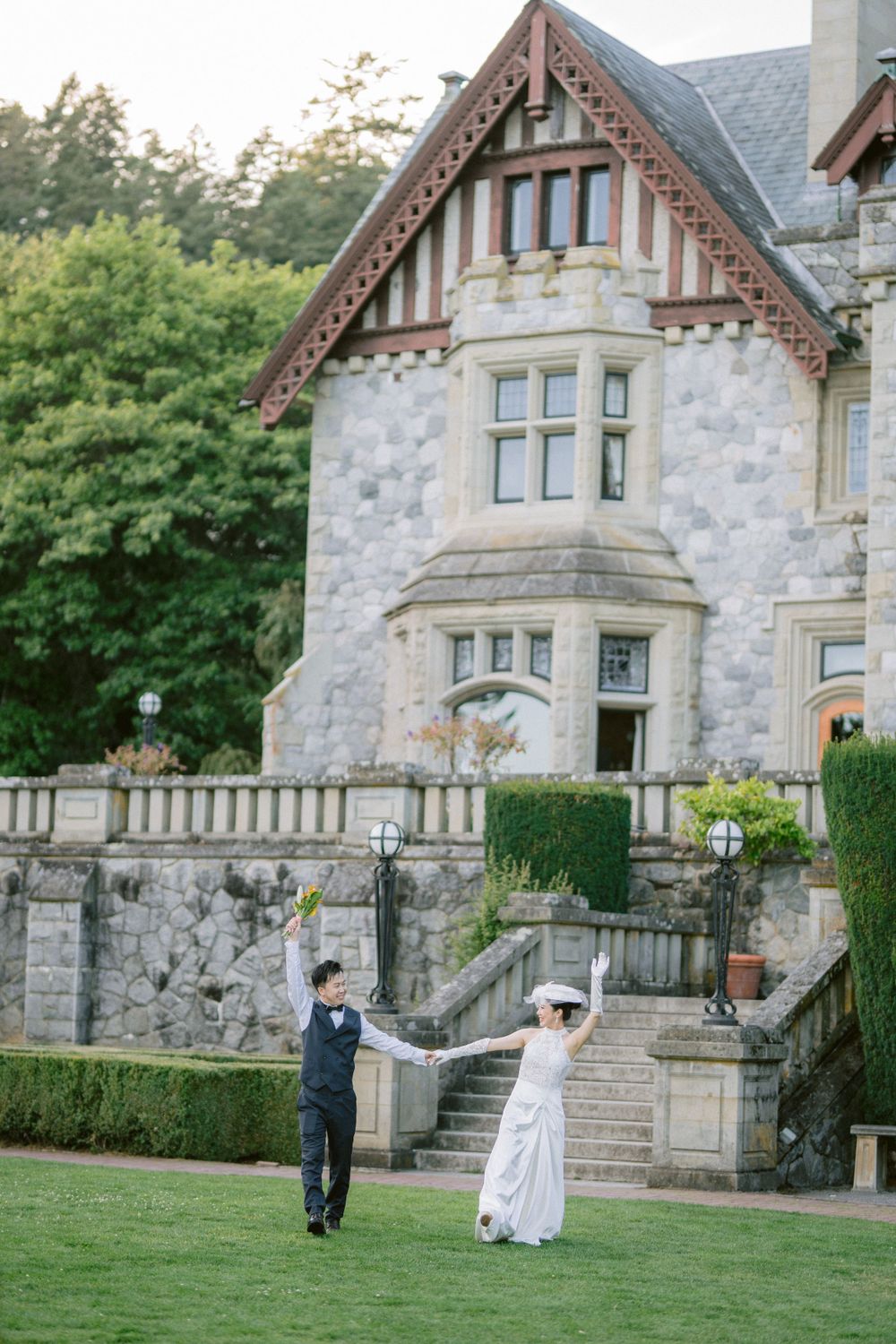 Joyful couple dancing on lawn in front of stone castle with manicured hedges.