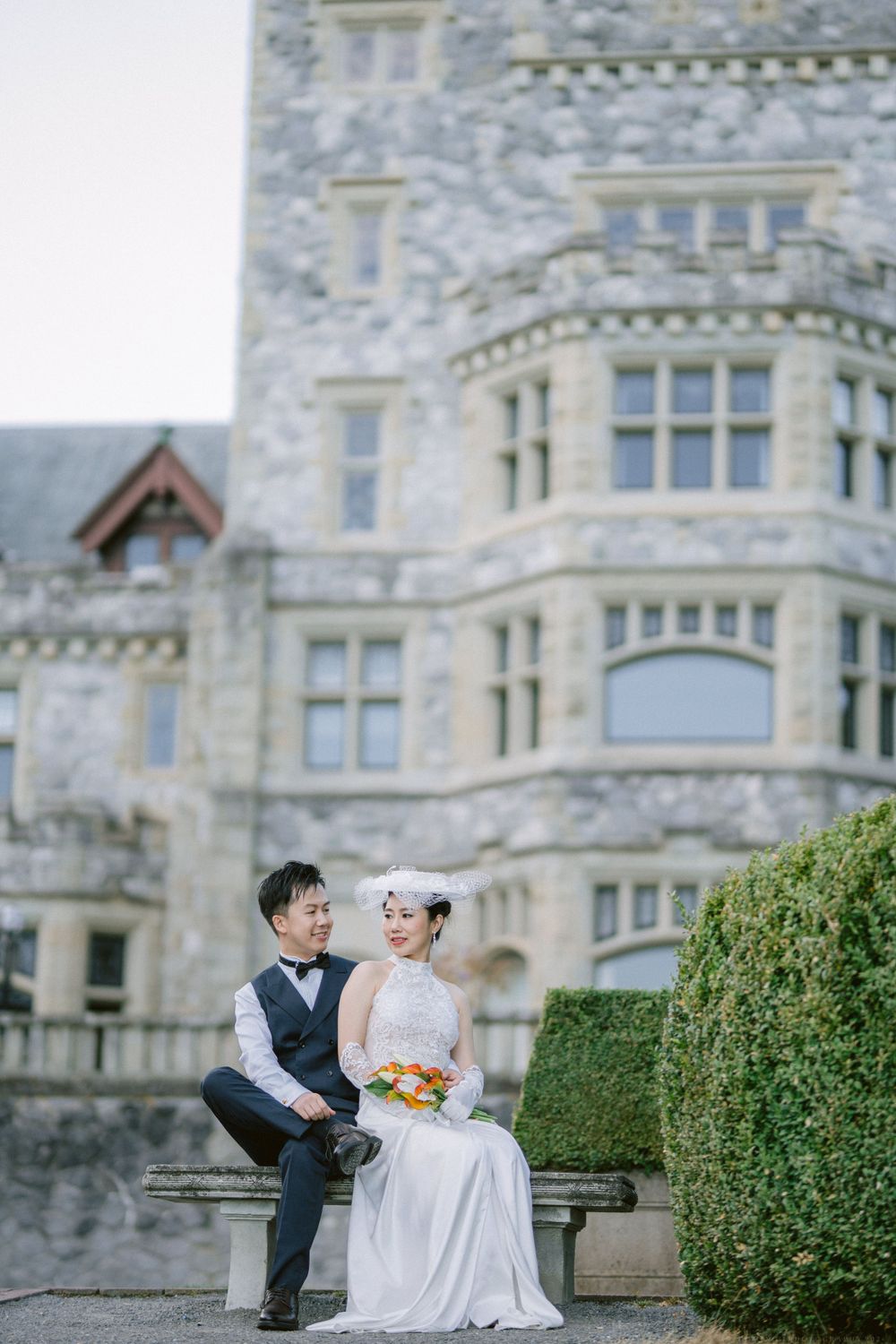 Couple sitting on bench against backdrop of Gothic stone castle architecture.