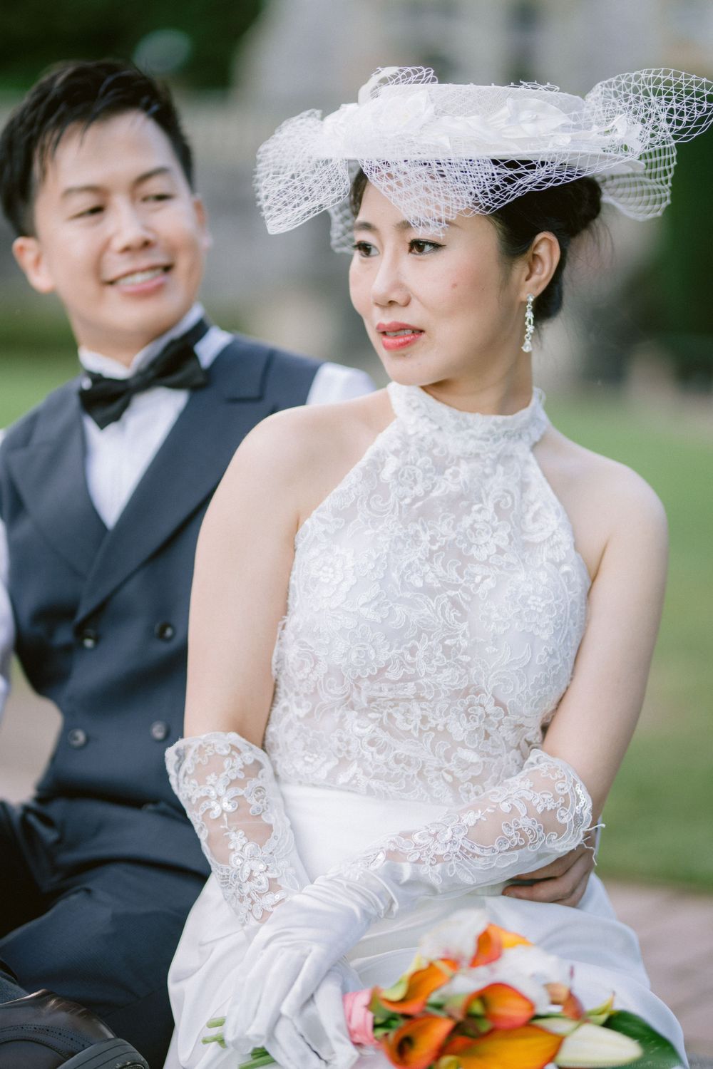 Wedding couple in formal attire with bride wearing vintage-inspired lace gown and ornate netted hat.