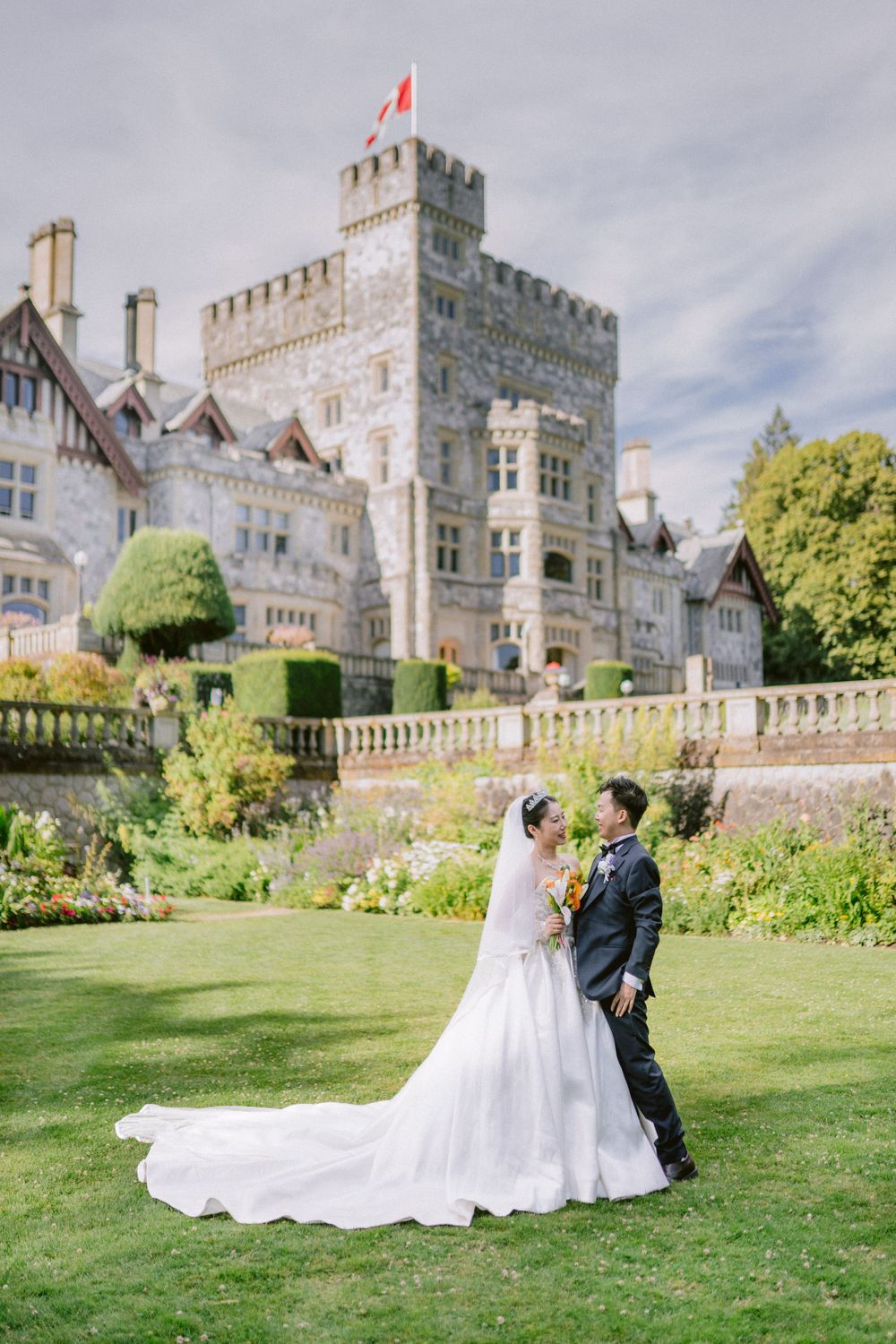 Wedding couple poses on manicured lawn with grand castle-style building in background.