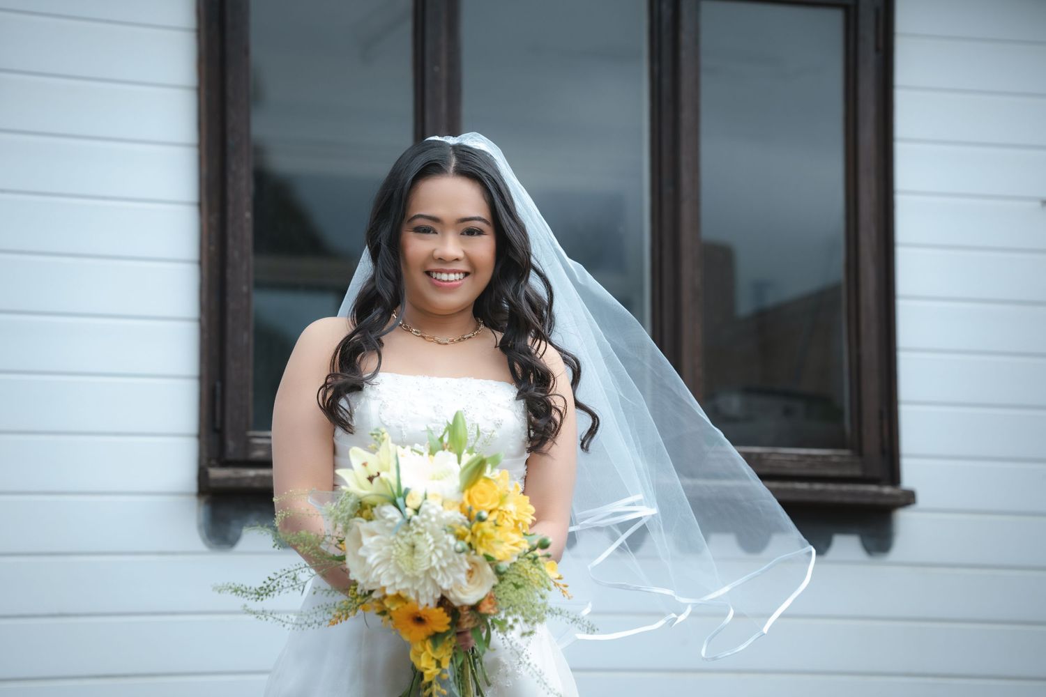 Elegant bridal portrait against white building with yellow and white bouquet.
