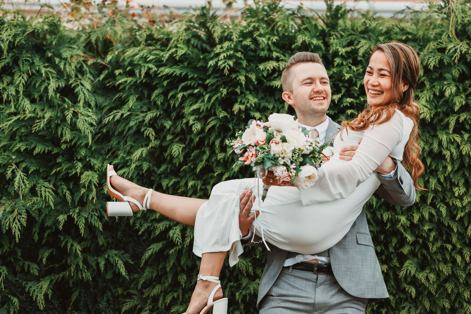 Joyful wedding couple embracing and dancing in an outdoor garden setting.