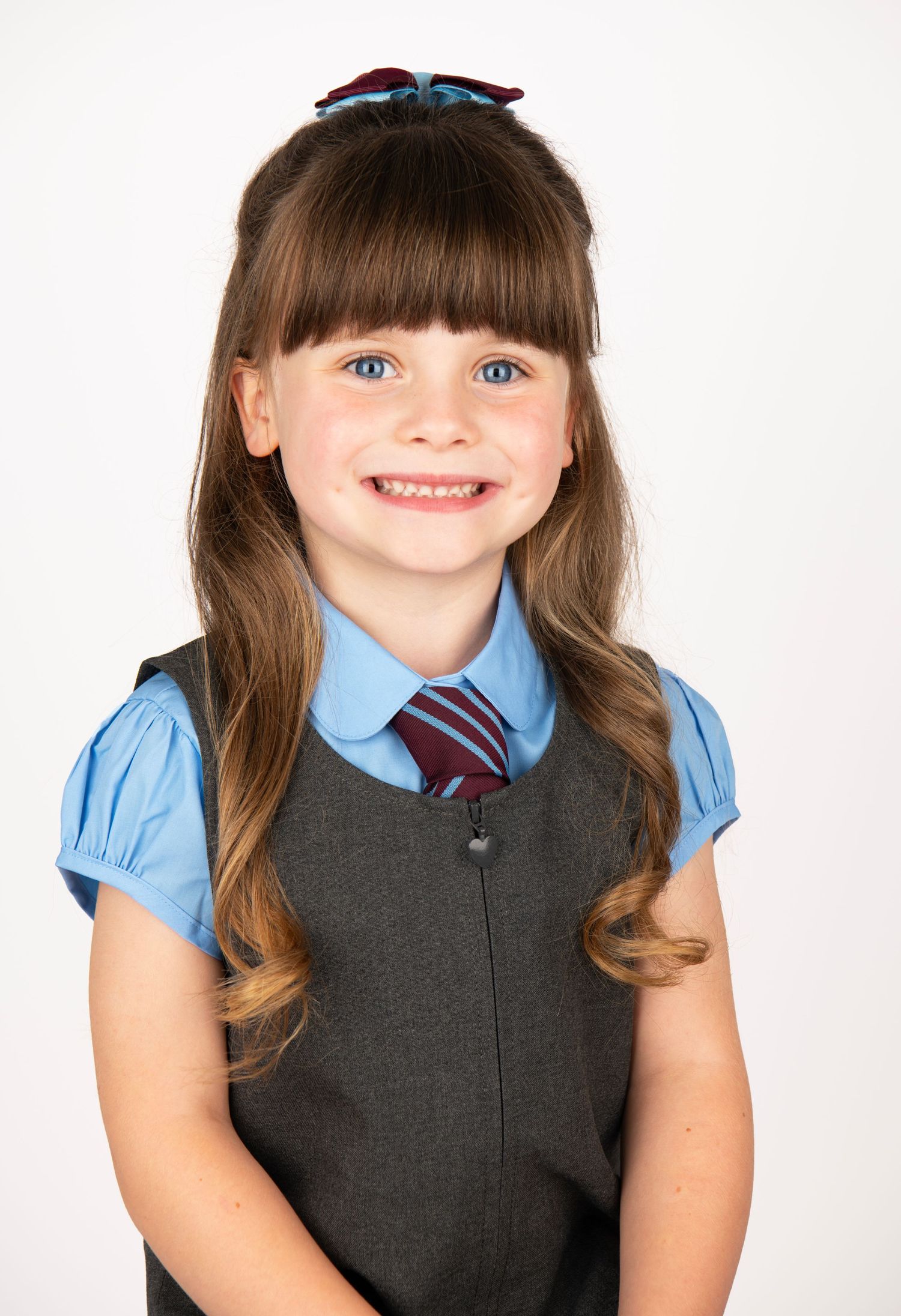 Child in school uniform with blue blouse, grey vest and striped tie.