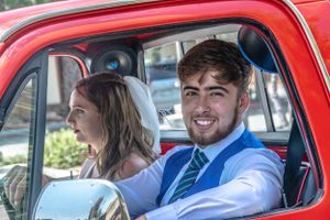 Happy couple sits together in a vintage red car.
