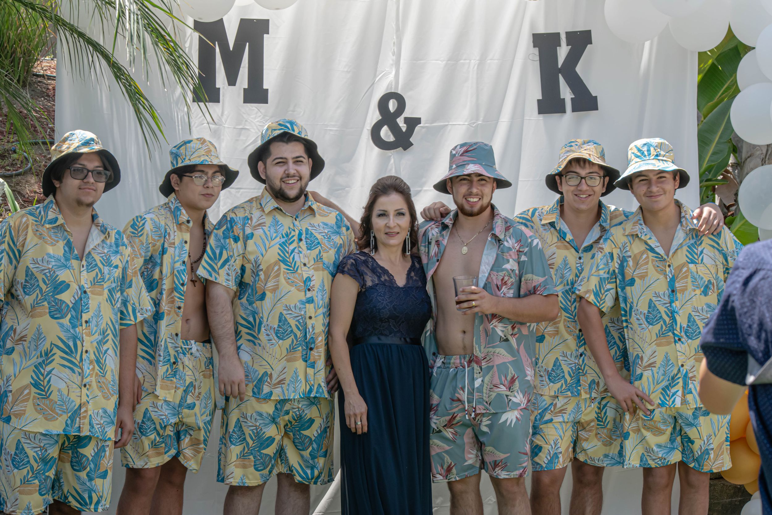 Wedding guests in matching tropical print shirts pose together outdoors.