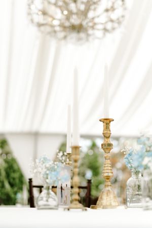 Gold candlestick and delicate blue flowers under white tent with crystal chandelier.