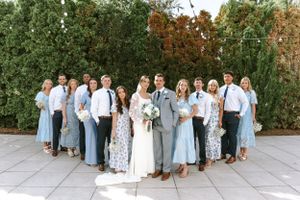 Wedding party lined up in coordinating light blue and white outfits against garden backdrop.