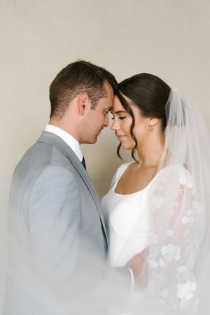 Intimate wedding portrait showing couple in tender moment with bride in veil and groom in gray suit.