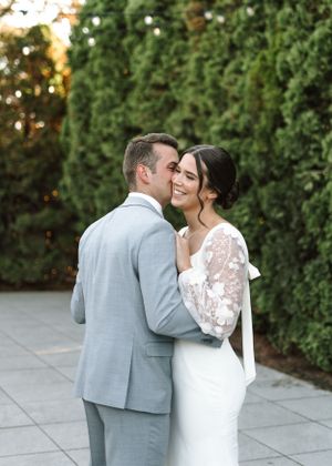 Tender moment between newlyweds with bride in lace sleeve dress and groom in light gray suit.