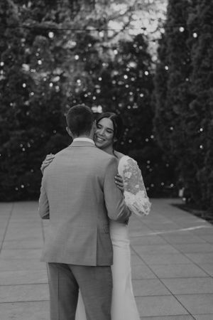 Black and white romantic portrait of couple dancing outdoors with twinkle lights in background.