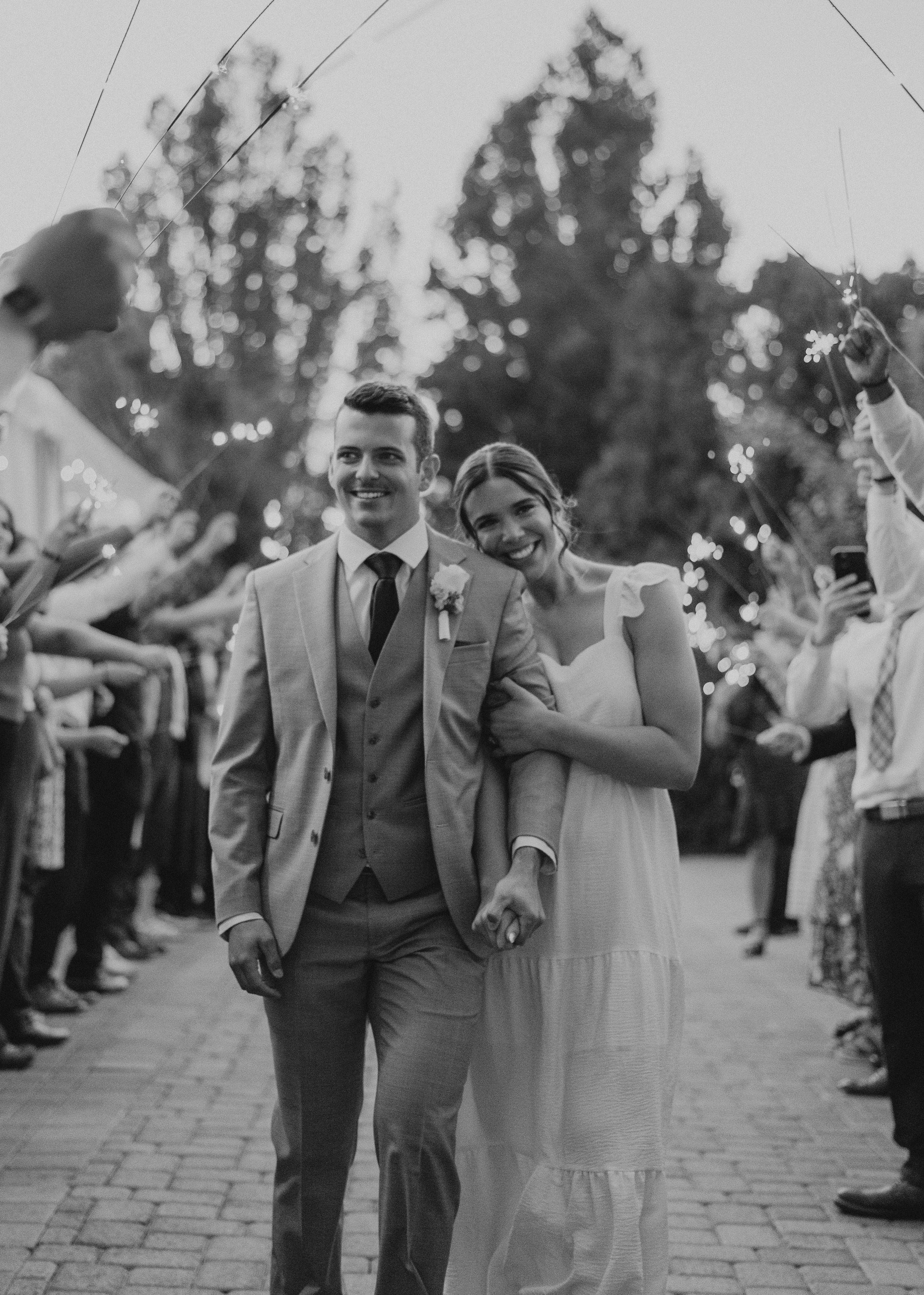 A black and white photo of a joyful couple walking down a path lined with wedding guests.