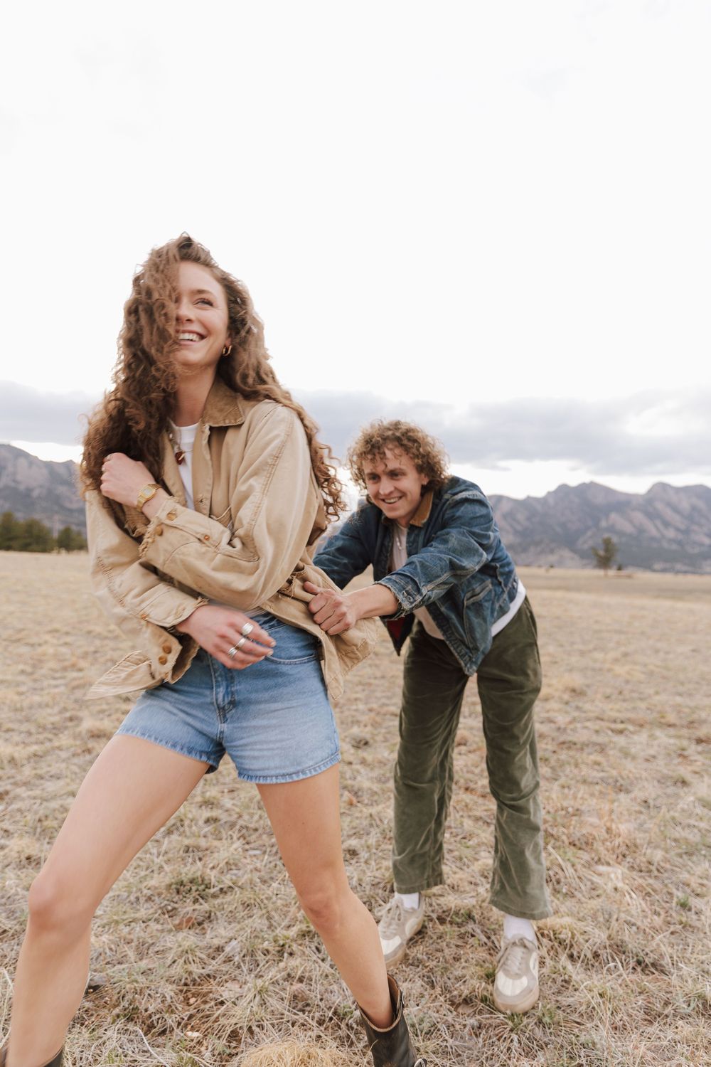 Two people having fun outdoors in a field with mountains in the background wearing casual clothes in autumn.