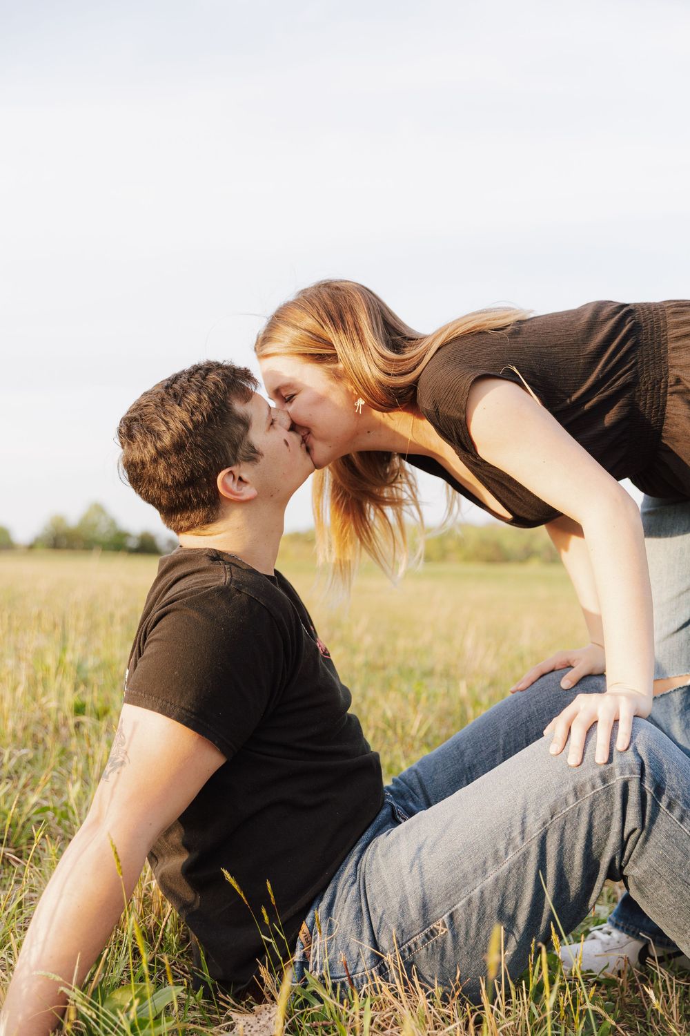 Romantic couple in casual attire lying together in a grassy meadow during sunset.