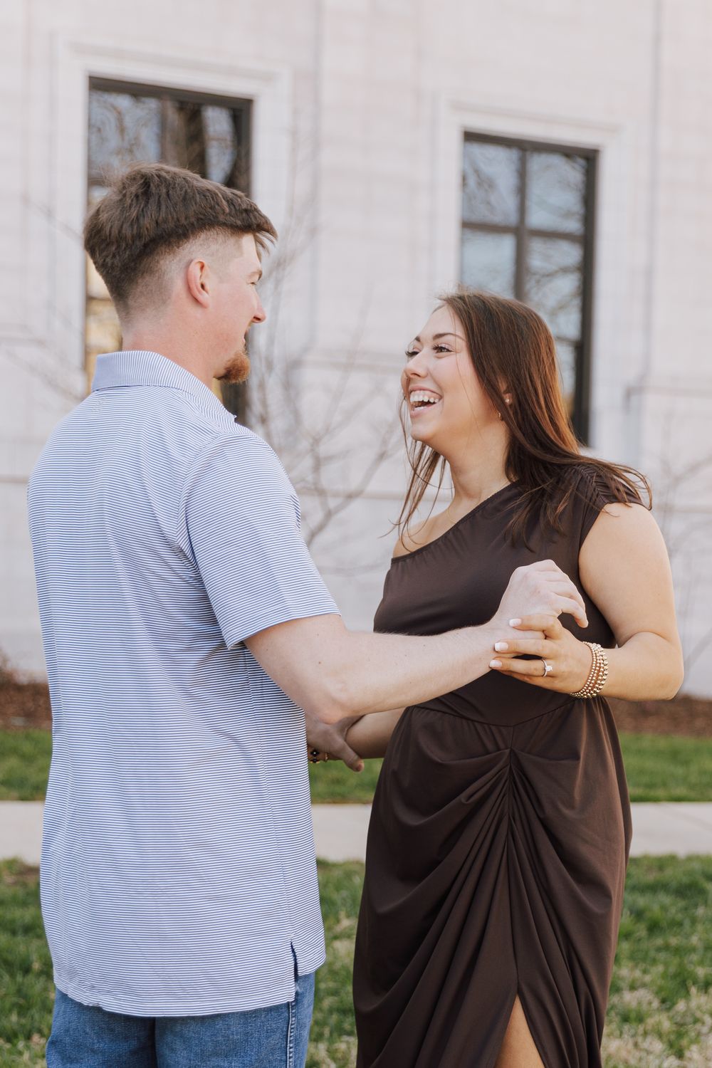 A couple shares a joyful moment outdoors as they stand close together, with one wearing a brown dress and the other in blue.