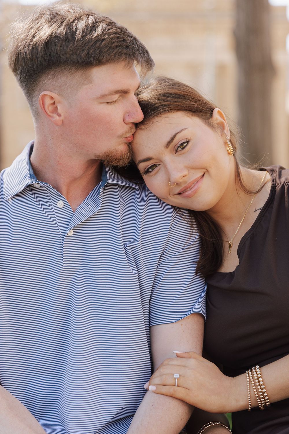 A romantic couple sharing a tender moment outdoors in natural lighting, with one person kissing the other's temple.