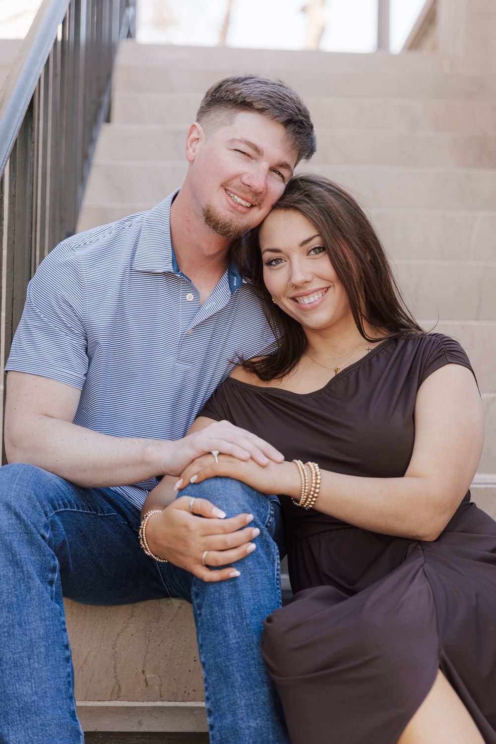 A couple sits together on concrete steps in a romantic maternity photoshoot wearing black and blue casual attire.