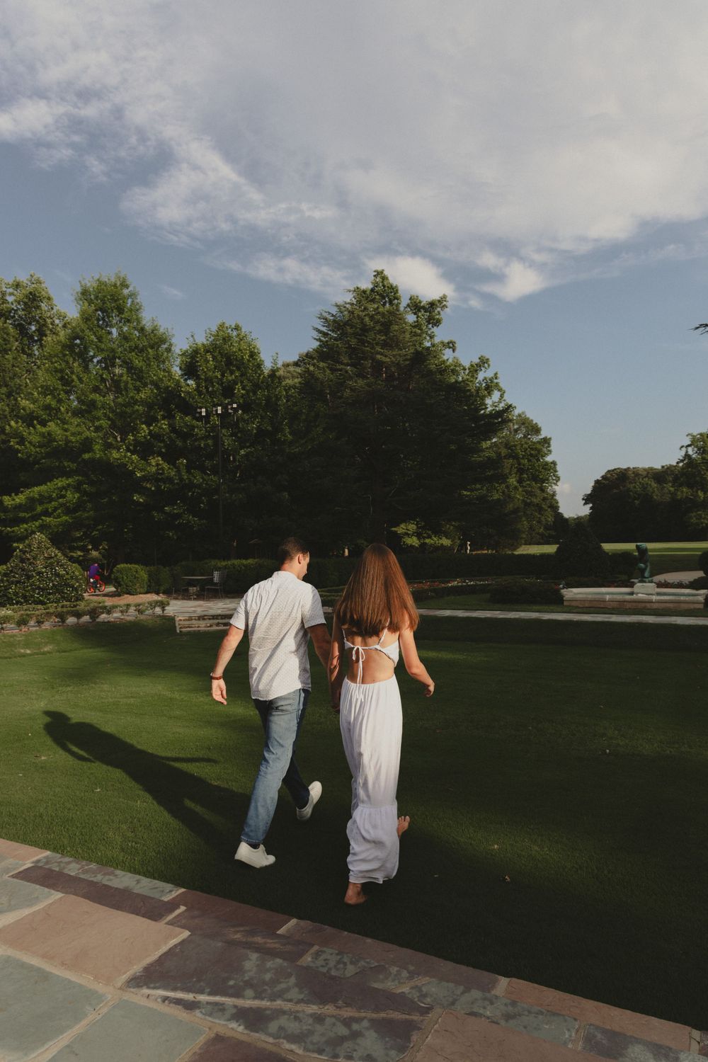 Two people walking together on a stone path beside a manicured lawn on a summer day.