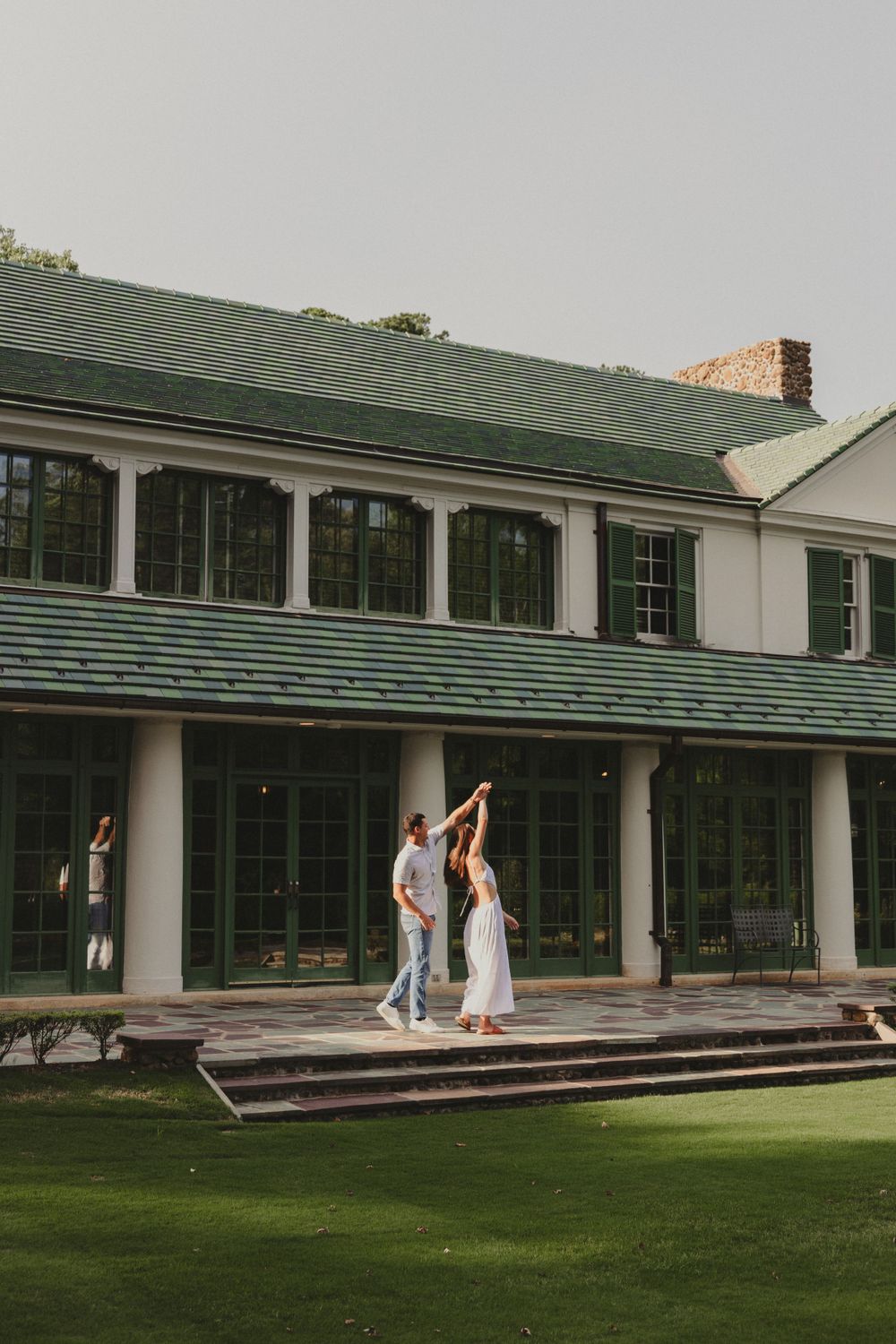 Two people dancing together on the patio of an elegant white mansion with green trim.