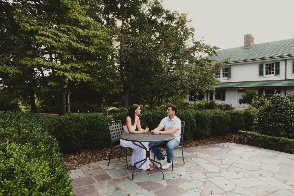 Couple sitting at outdoor table in garden setting having conversation.
