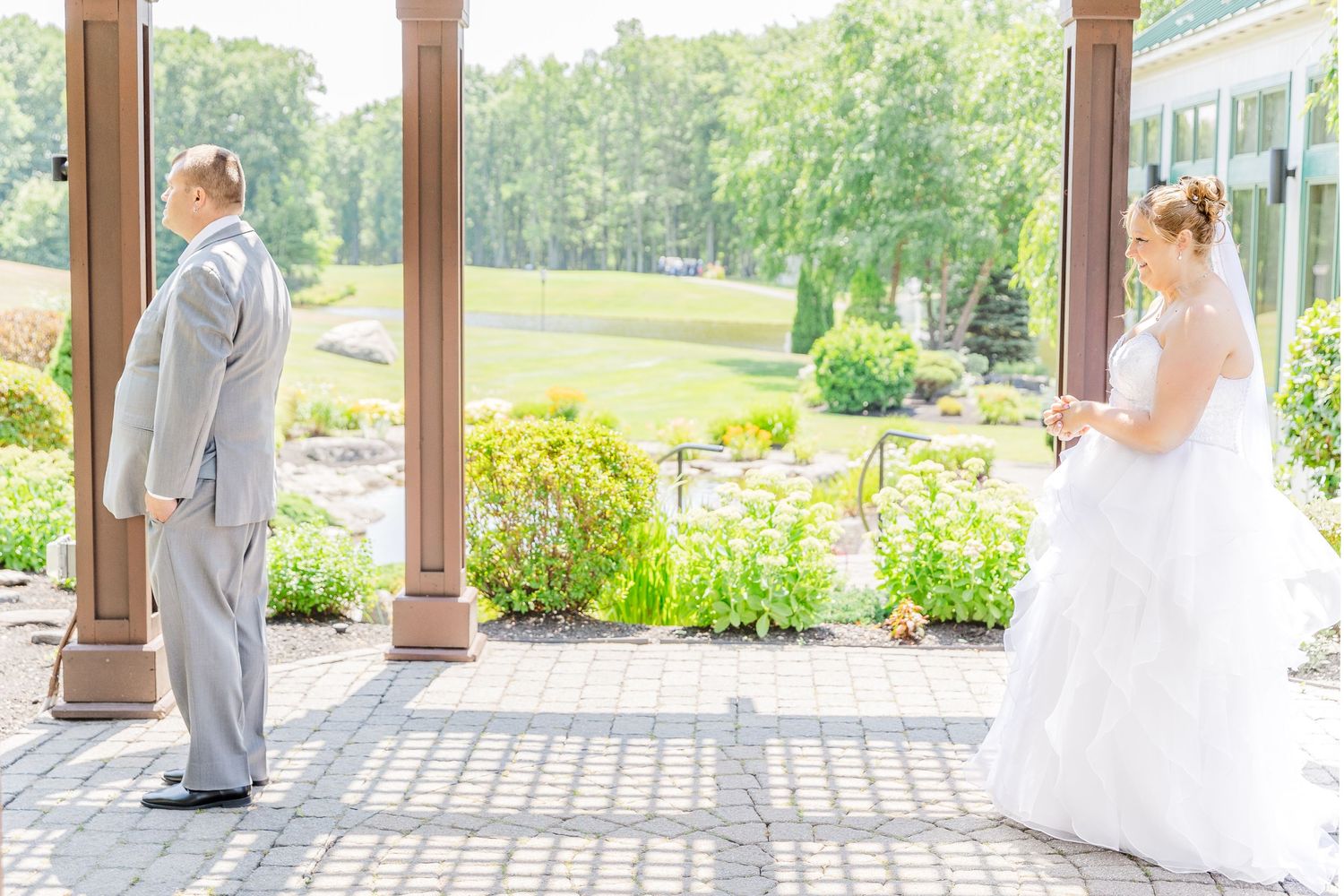 A couple shares their first look moment on a covered porch surrounded by lush gardens and columns.