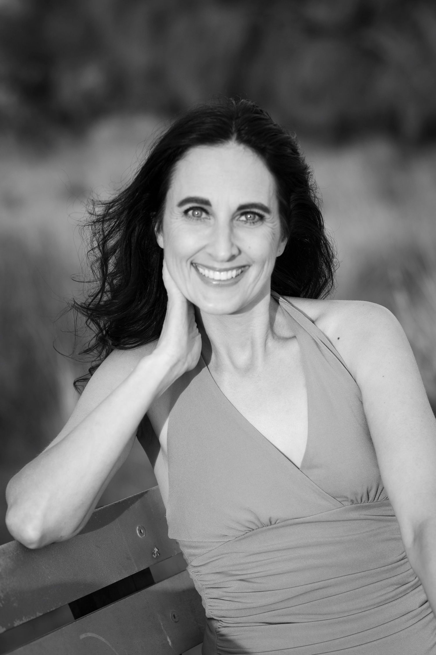 Black and white portrait of smiling dark-haired woman in halter dress outdoors.