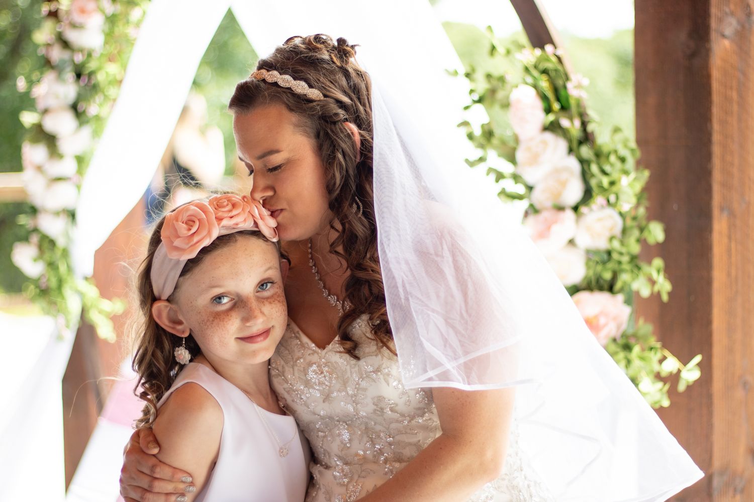 Bride kissing flower girl on the head at her wedding. Flower girl smiling at camera.