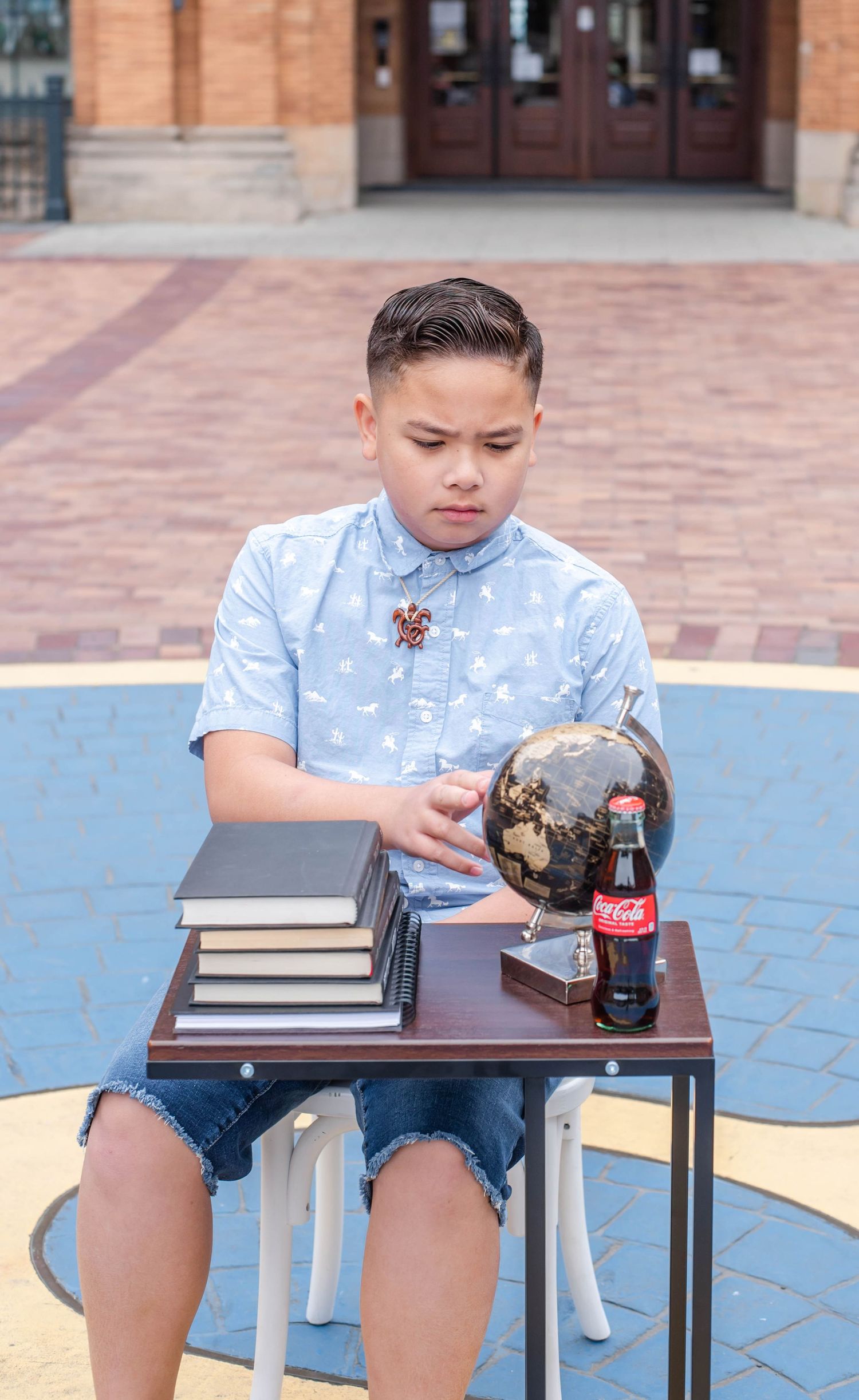 Student in light blue shirt studies at small table with books and Coke bottle.