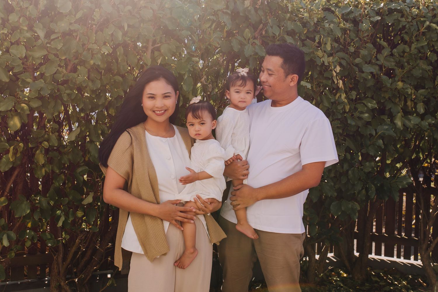 A tender family portrait taken outdoors against a leafy garden backdrop.