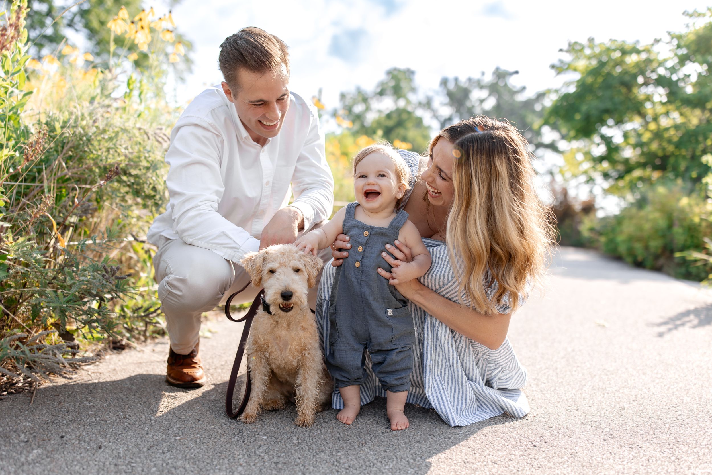 Family moment on garden path with fluffy dog and joyful expressions.