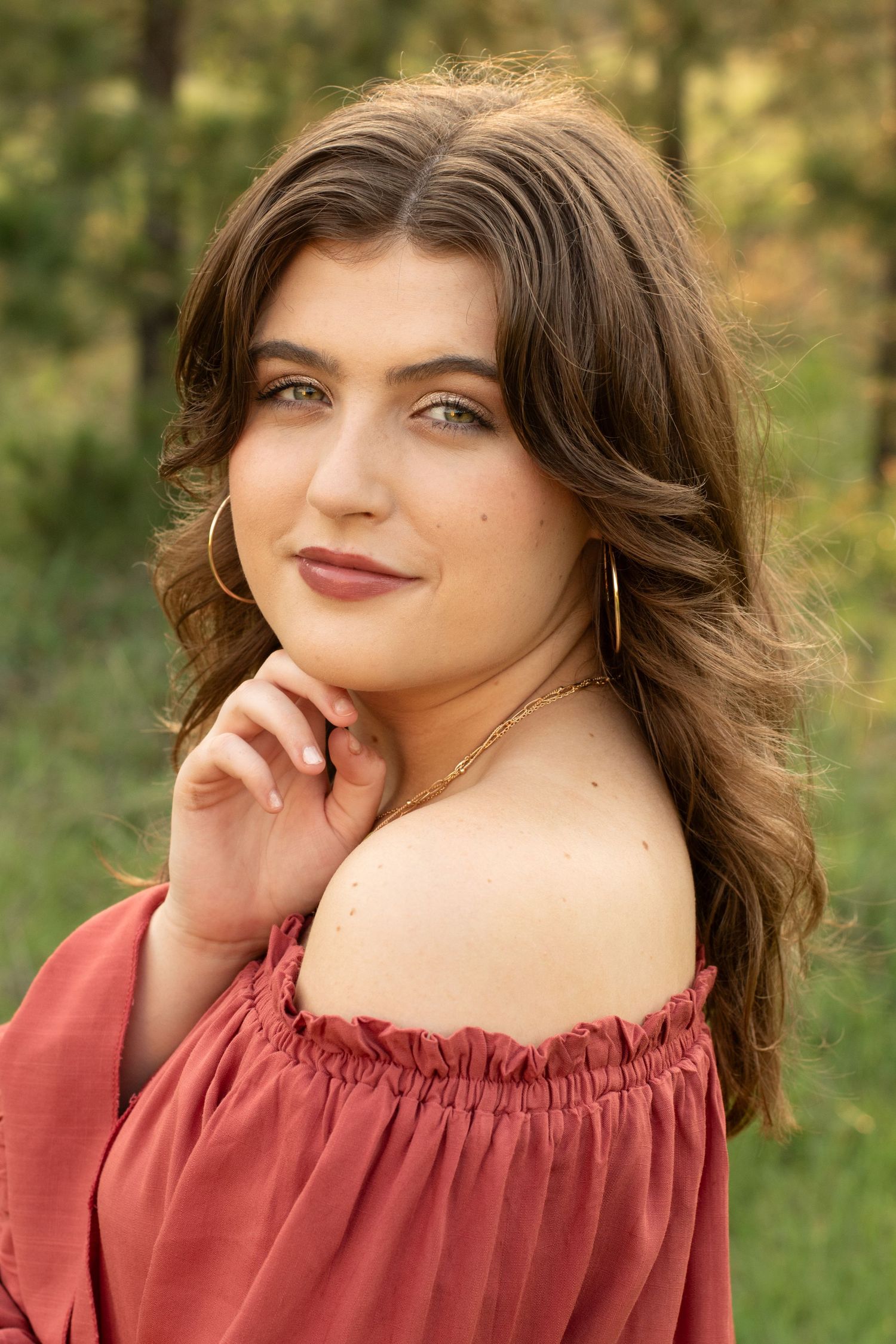 Portrait of woman in coral off-shoulder top posing against natural forest background.
