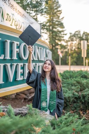 Graduate celebrating with raised cap in front of California university sign.