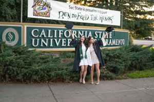 Graduates celebrating in front of California State University Sacramento sign.