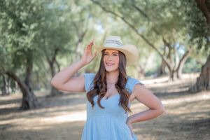 Summer portrait in blue dress and sun hat against natural outdoor setting.
