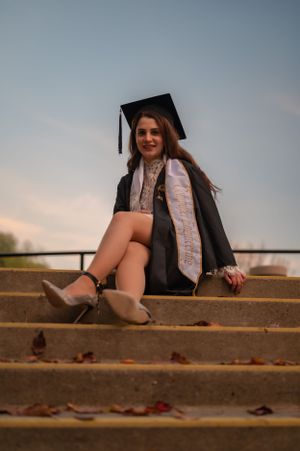 Graduate in cap and gown sits on outdoor steps during sunset photo session.