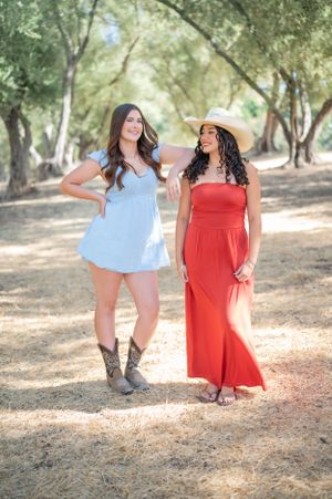 Two friends pose together on a woodland path wearing summer dresses in red and light blue.