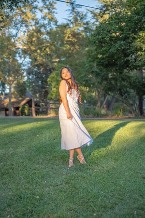 Elegant white dress twirls in golden afternoon sunlight on a lush green lawn.