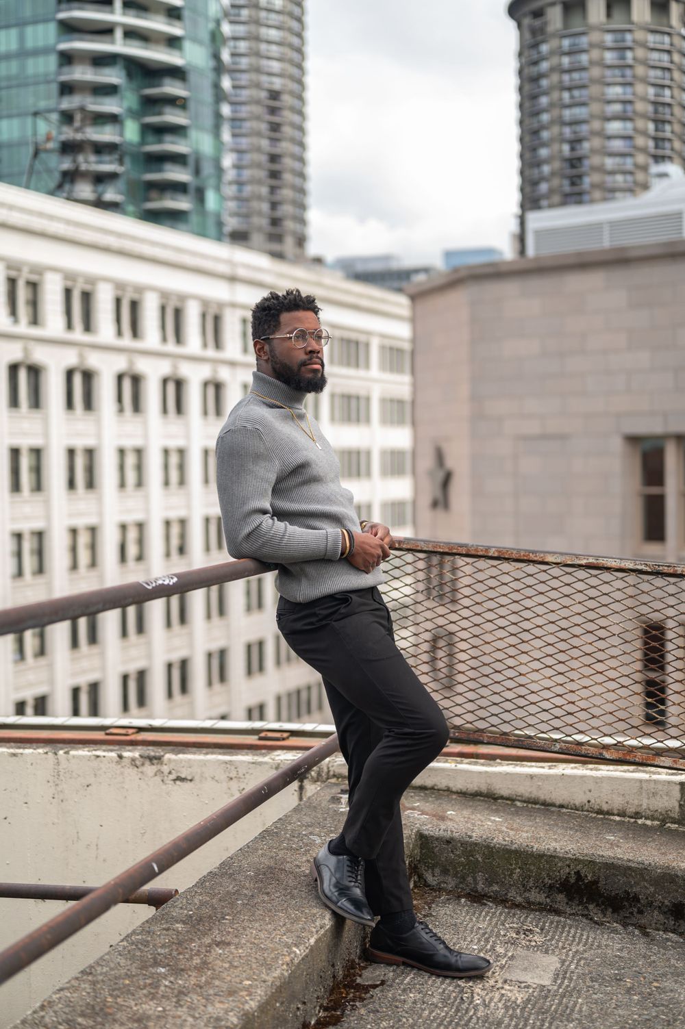 A casual urban portrait on a rooftop with city buildings and modern architecture in view.