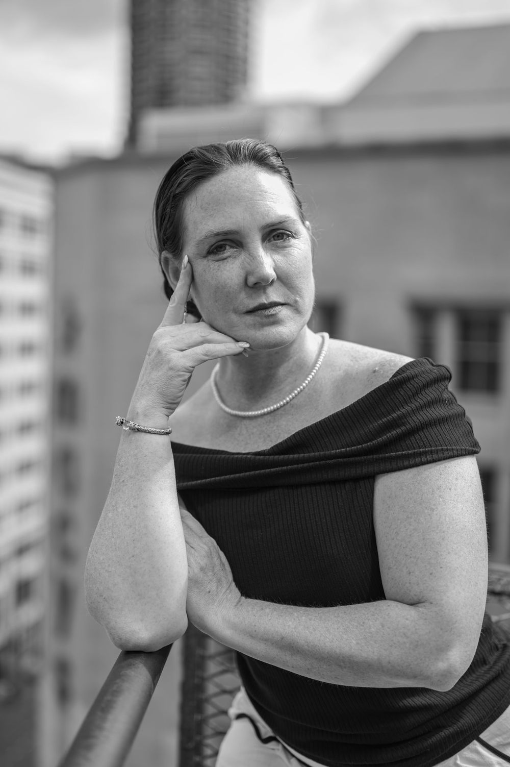 Portrait of woman in black off-shoulder top against urban backdrop.