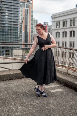 Woman in flowing black dress twirling on urban rooftop with city buildings behind.